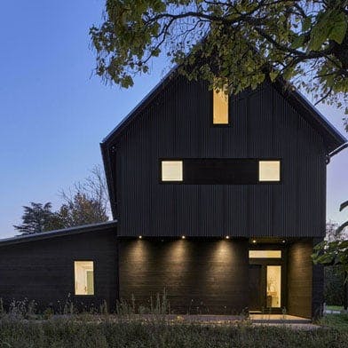 A black barn-style home silhouetted against an evening sky. 