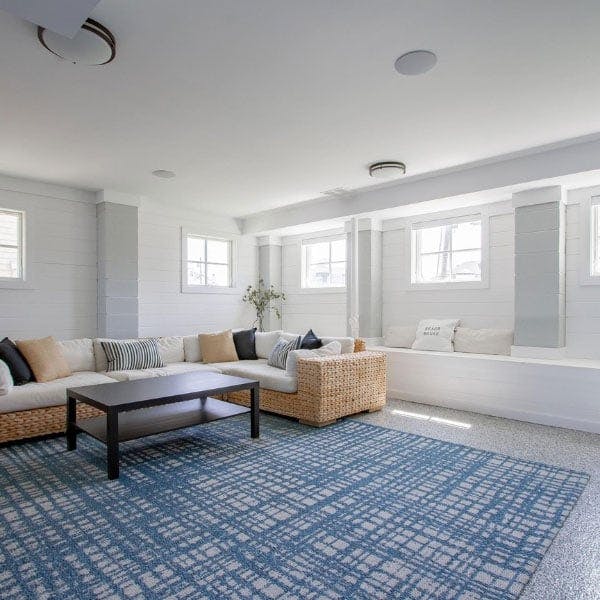 A beachy blue and white themed basement flooded with natural light from the white picture windows with grilles.