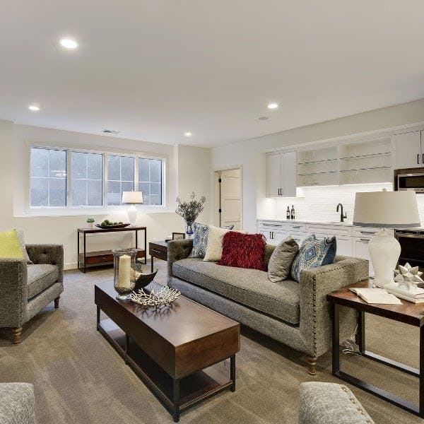 A white painted basement flooded with light from the white picture windows with grilles in a living room with a modern gray couch and coffee table.