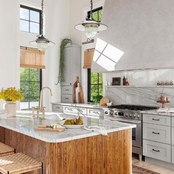 A farmhouse kitchen with white concrete countertops, stainless steel appliances and walnut center island surrounded by black windows with grilles bringing in loads of sunlight.