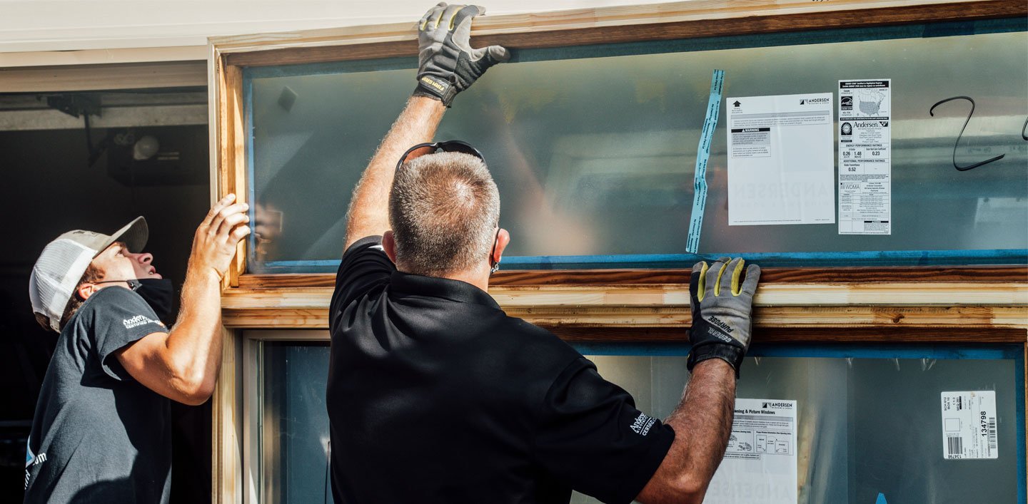 Two Andersen Certified Contractors installing a large wooden window.