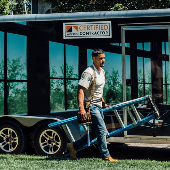 Andersen Certified Contractor carrying a ladder in front of trailer