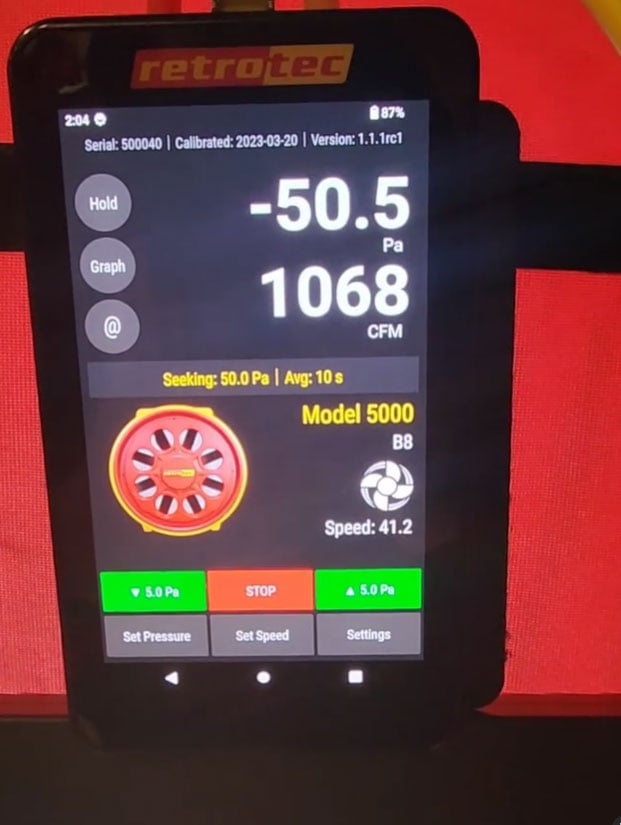 Close-up view of a digital control screen for a Retrotec Model 5000 blower door system. The screen displays a pressure reading of -50.5 Pascals and an airflow measurement of 1068 cubic feet per minute (CFM). Various control buttons are visible, including 'Set Pressure,' 'Set Speed,' 'STOP,' and 'Settings.'