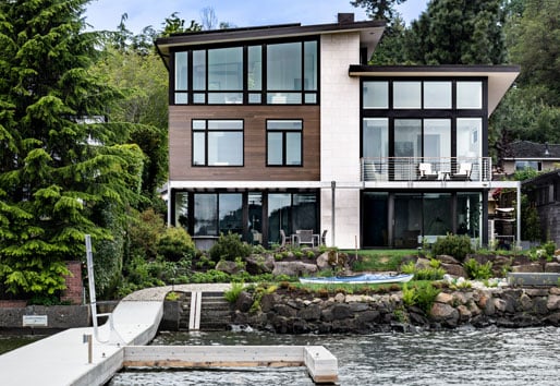 An exterior shot of a contemporary home with a combination of siding types, large expanses of glass, and a lakeside location.