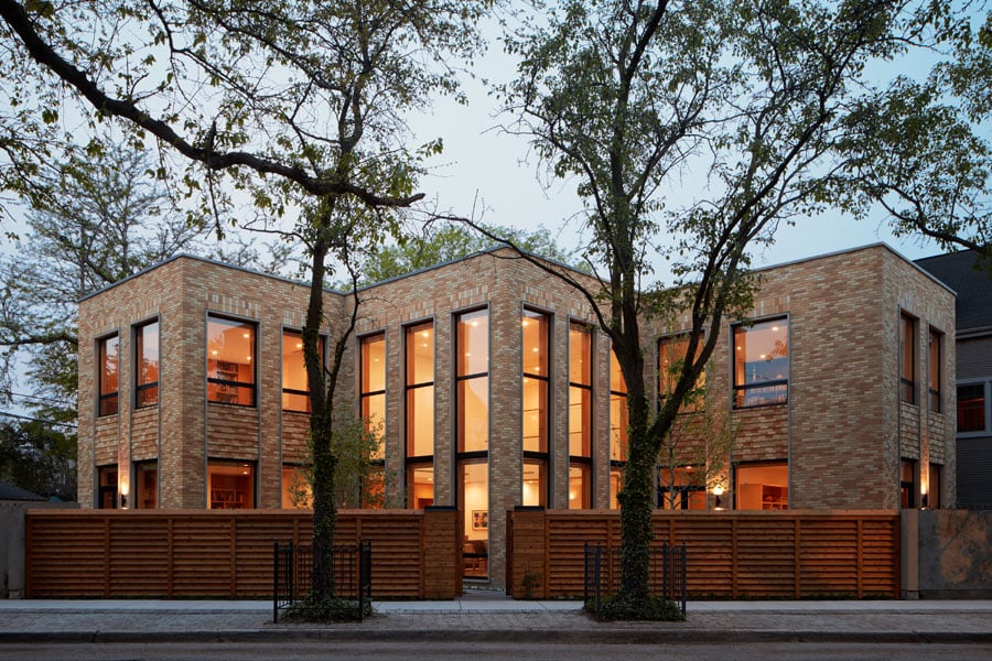 An exterior view of a brick, two-story home with prominent floor-to-ceiling windows.