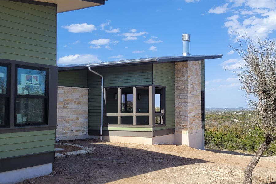 A house during construction with sage green siding, an awning, and Andersen windows.