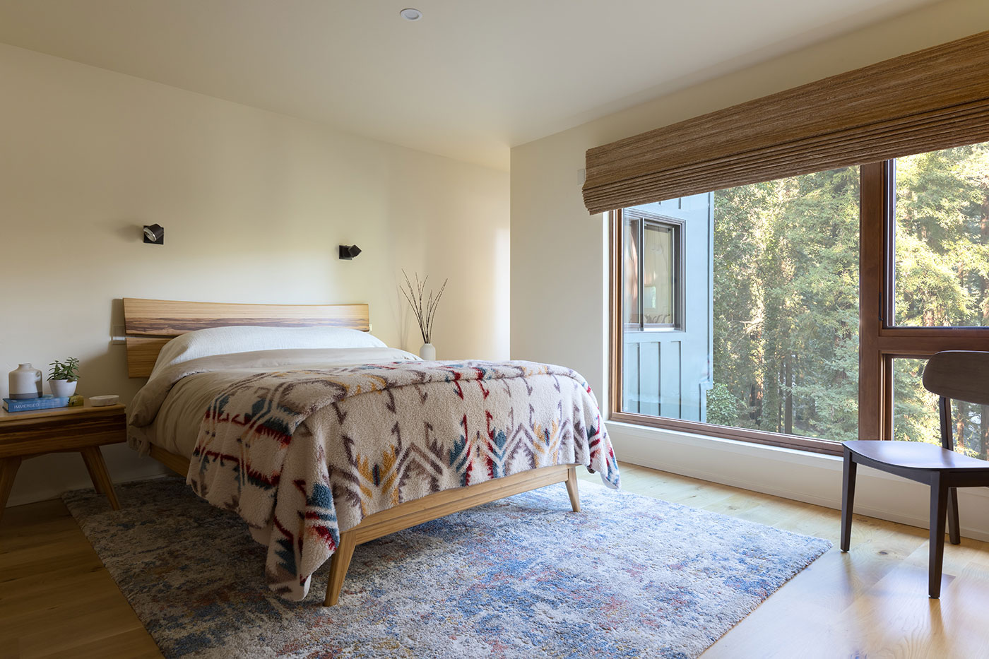 A bedroom with a large window combination showcasing views of redwood trees outside.