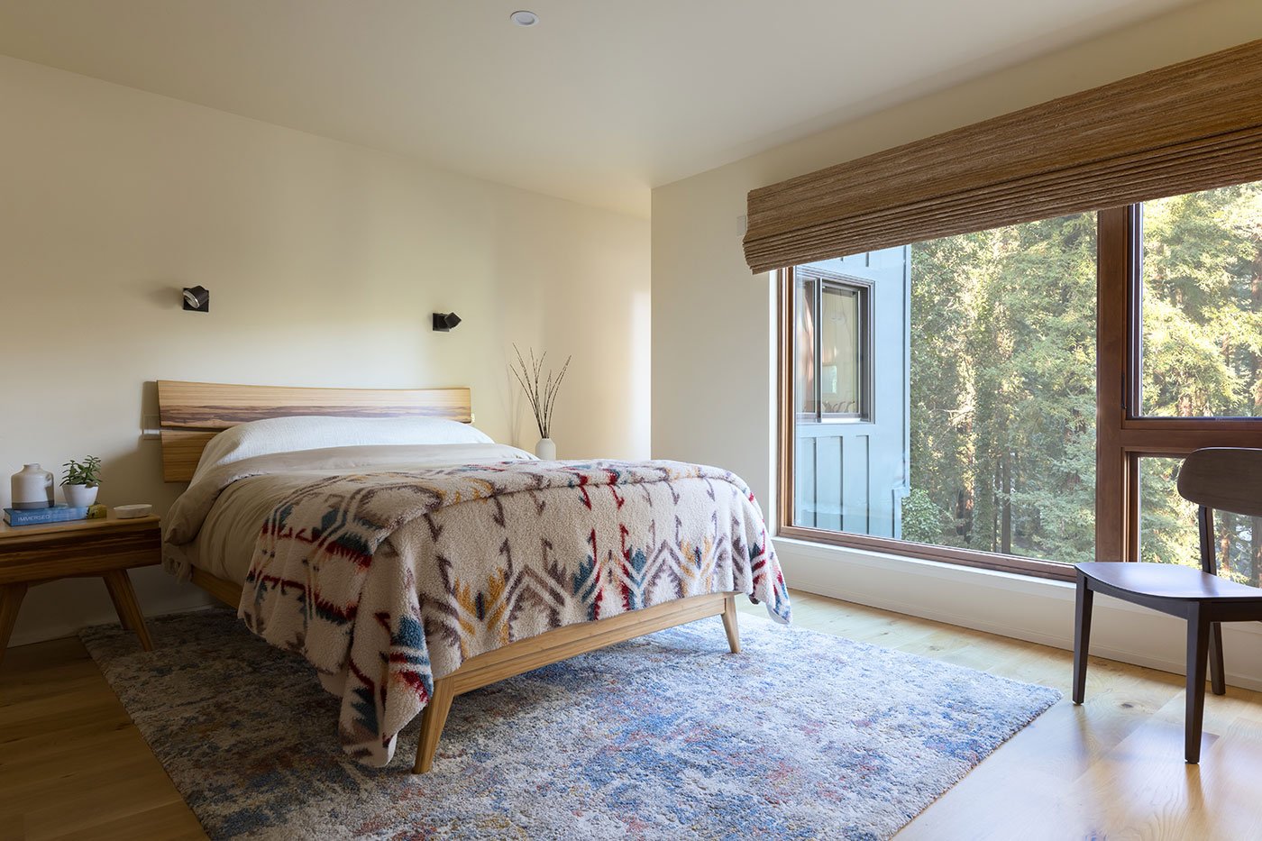 A bedroom with a large window combination showcasing views of redwood trees outside.