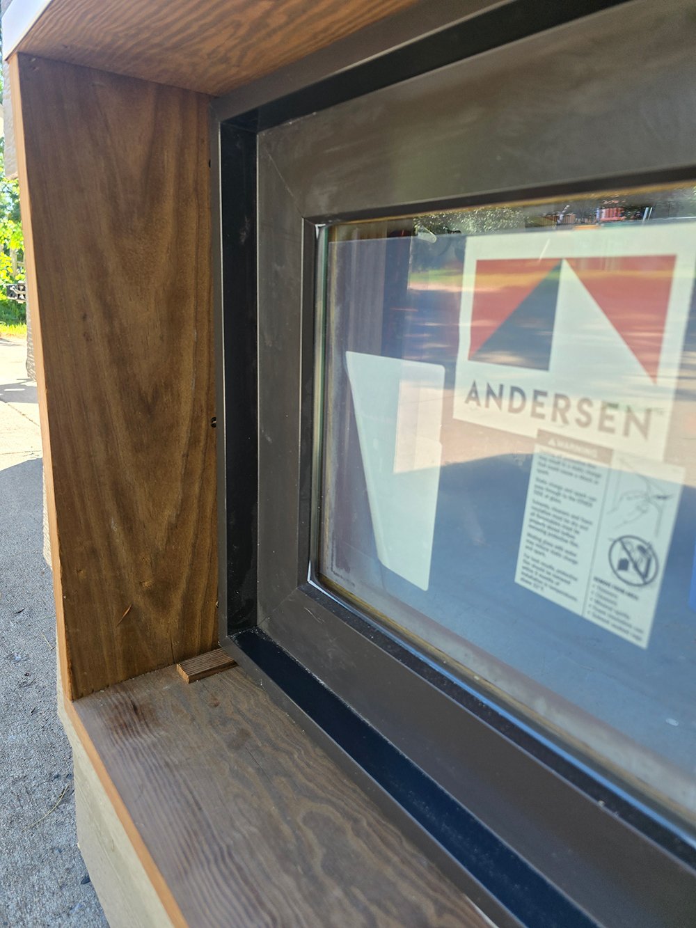 A black innie window with an Andersen sticker sits inside its wood rough opening.