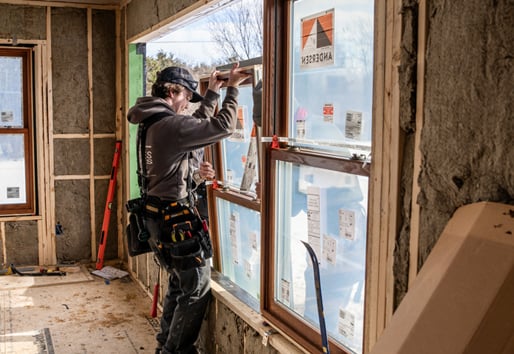 A man installs a window with Andersen stickers inside a new home build. 