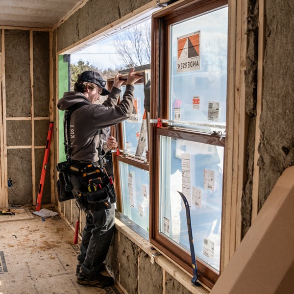 A man installs a window with Andersen stickers inside a new home build. 