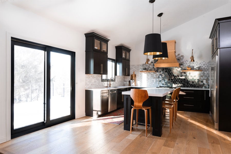 A black-framed gliding patio door in a kitchen with black cabinetry, center island, and statement black-and-white tile.