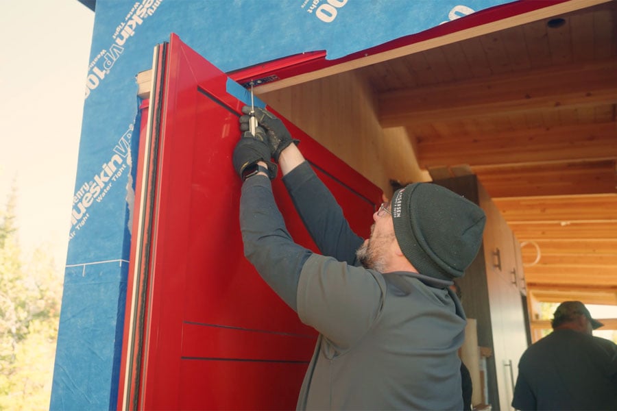 A man uses a screwdriver to lower the top pin from a door frame to the Pivot Door panel.