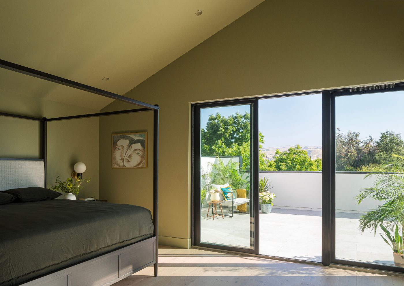 A bedroom with a black gliding patio door leads to a patio area with plants and furniture.