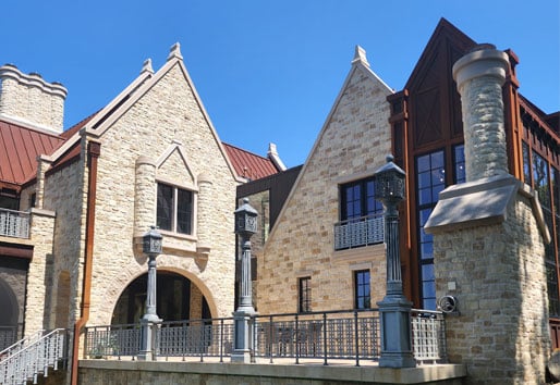 a stone building with gothic architectural features, including pointed arches, decorative columns and steeply pitched roofs. The building has multiple levels, large windows and a mix of stone and wood elements