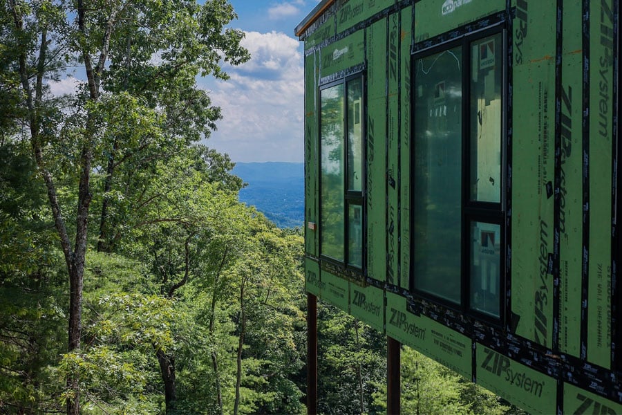 An under-construction mountainside home covered in Zip System WRB stands on stilts among the trees.