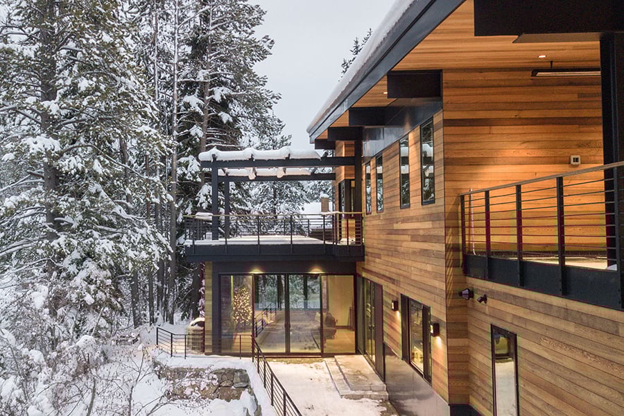 Stunning wood siding home with many large black framed windows, and grand porch with top deck