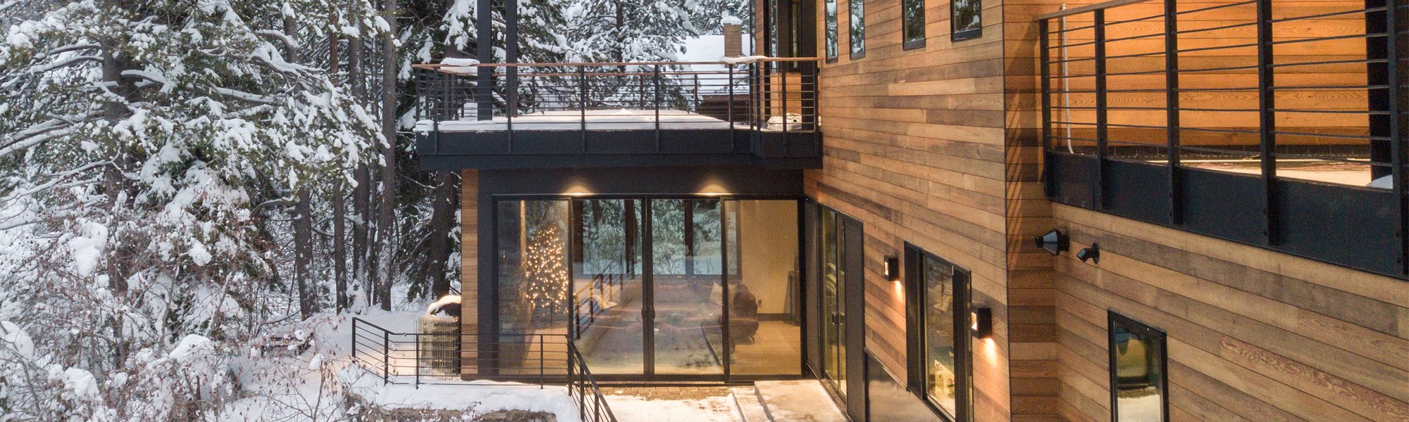 Stunning wood siding home with many large black framed windows, and grand porch with top deck