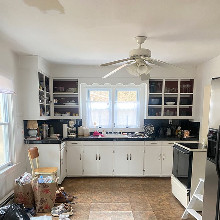 kitchen with two windows over the sink, white cabinets, and items strewn across the brown floors
