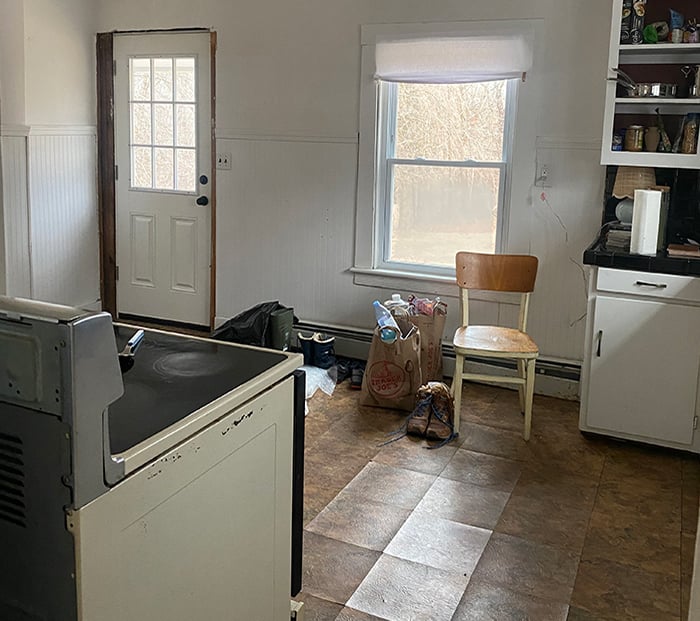 corner of a kitchen with a hinged door, double hung window and ceiling fan, and brown floors