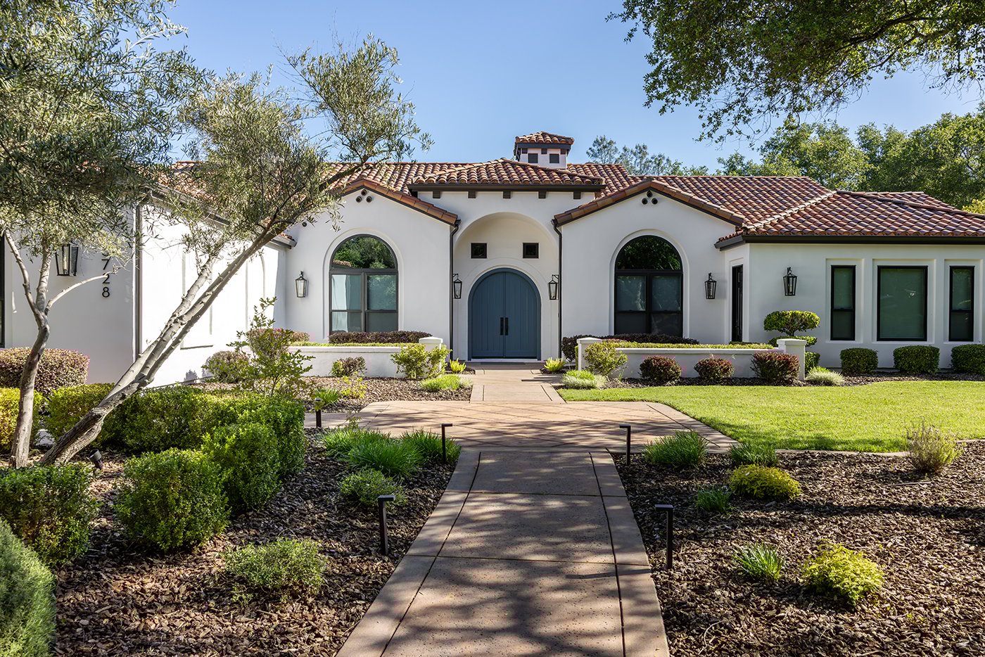 A Spanish-style home with circle-top windows, an arched front door and red tile roof.