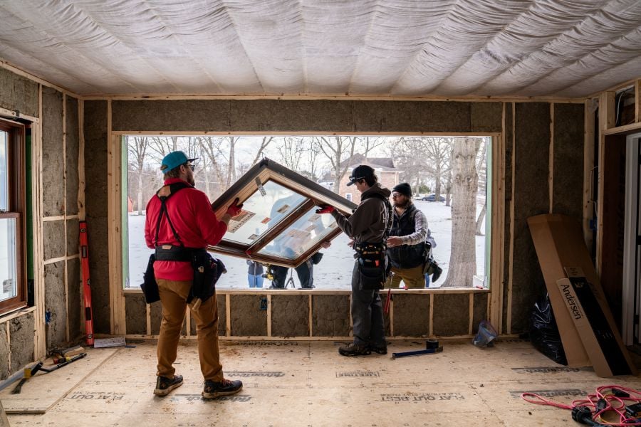 Four men install a window in a large opening of a home with snow outside.