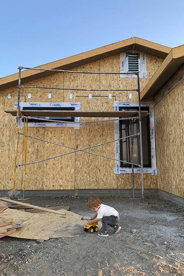 child kneeling in front of new construction home with black framed andersen windows