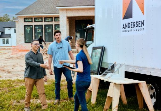 Two builders on a construction site greet a woman.