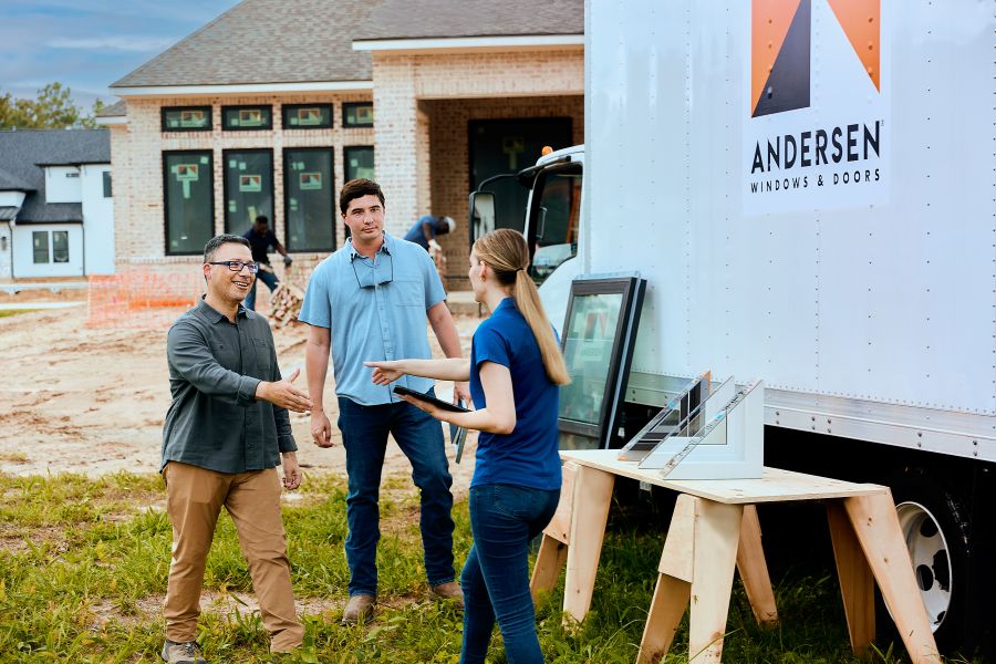 Two builders on a construction site greet a woman.