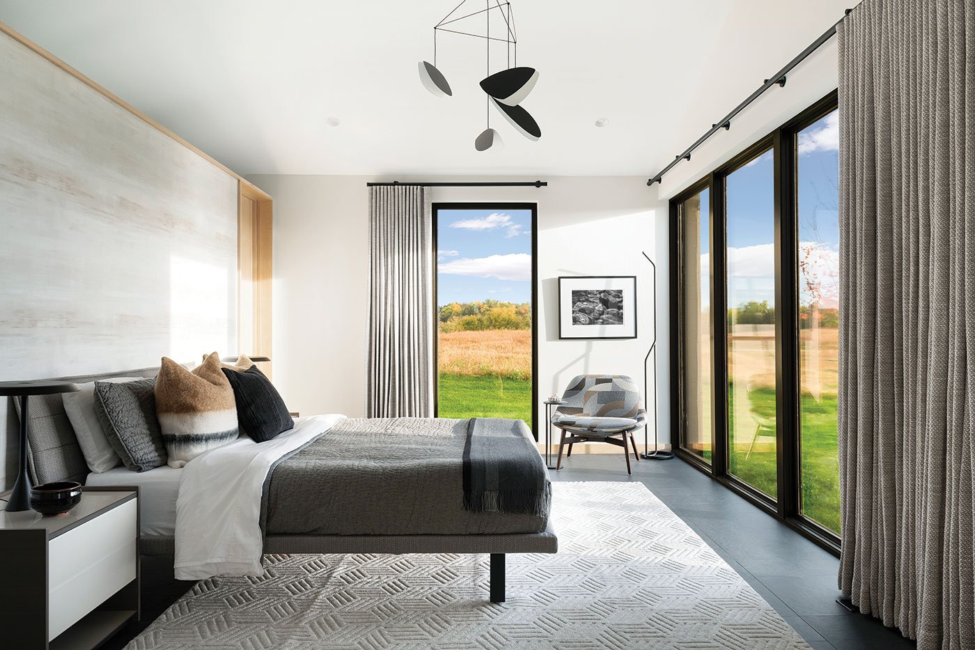 A bedroom with a black, white, and gray color scheme and contemporary aesthetic that includes two walls with floor-to-ceiling windows.