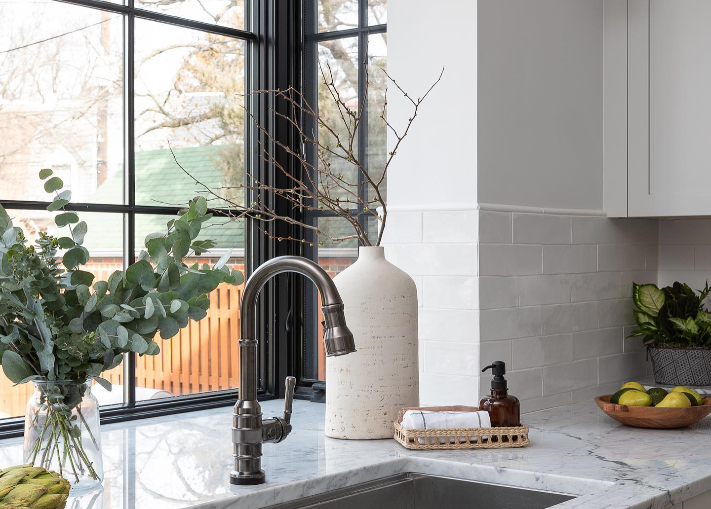 A garden window with black frames and colonial grilles in a kitchen with marble countertops and subway tile.