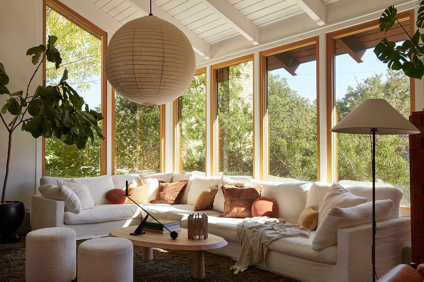 A living room in a mid-century home with white-oak framed windows that wrap around a corner and stretch from the floor all the way up to the ceiling.