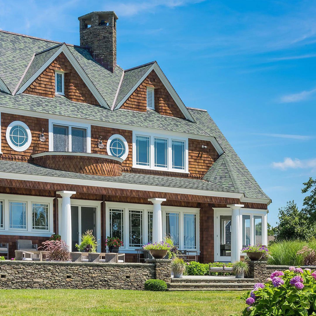 A two-story home with brown shingles, a porch with white columns, and white windows.