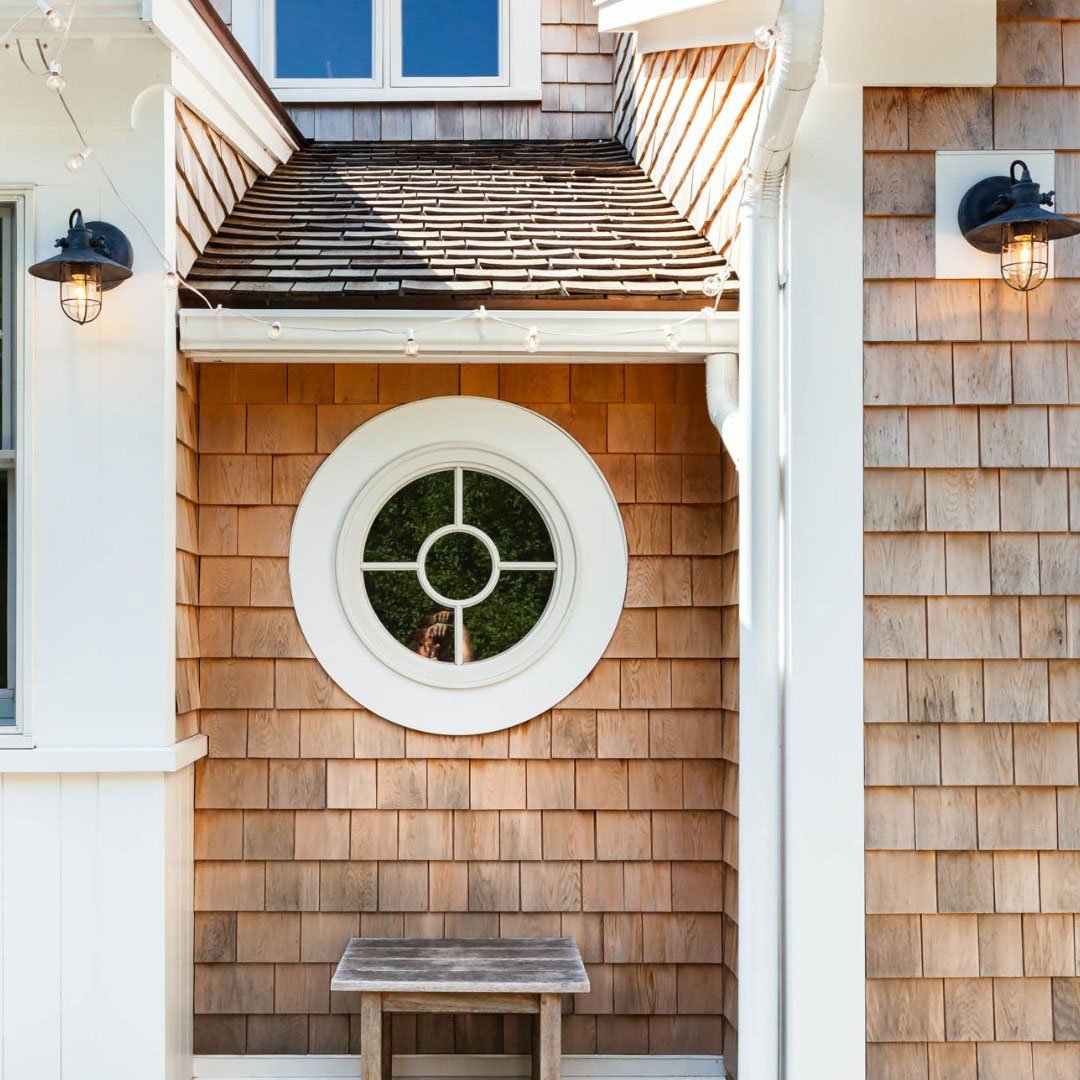 A two-story home with brown shingles, a porch with white columns, and white windows.