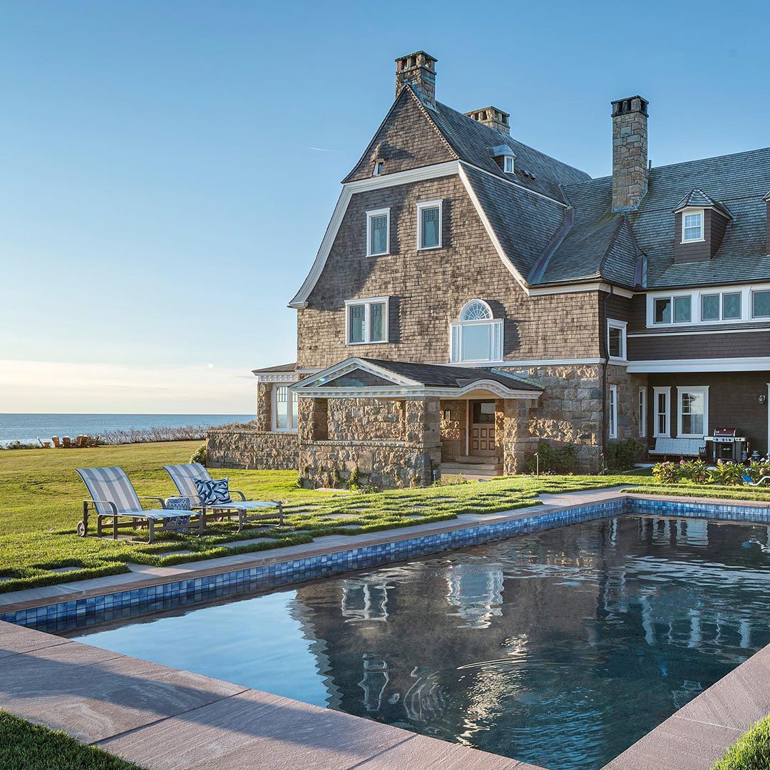 A two-story home with brown shingles, a porch with white columns, and white windows.
