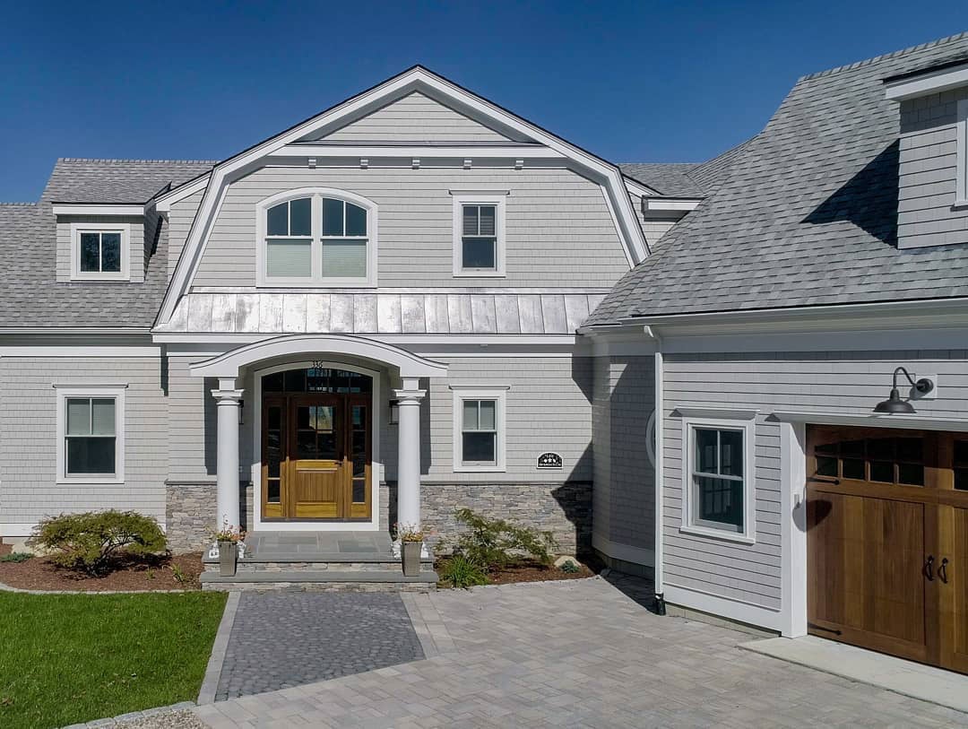 A two-story home with gray siding with white andersen windows.