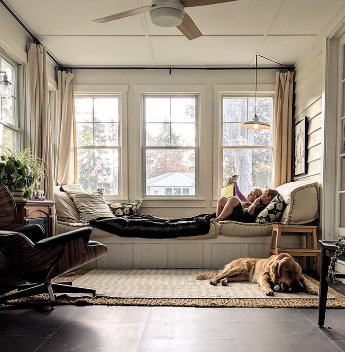 children lounging on a bench in the sunroom reading a book with a Golden Retriever at their feet