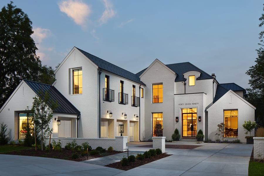 The front of a modern Tudor house with a three-door garage, white stucco, and narrow windows with black frames and colonial grilles. 