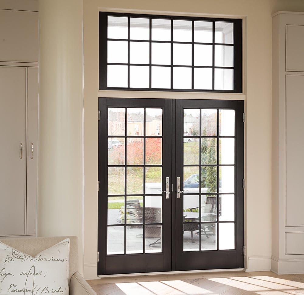 An interior shot of a black A-Series Hinged Patio door with a transom window and rectangular grille pattern. 