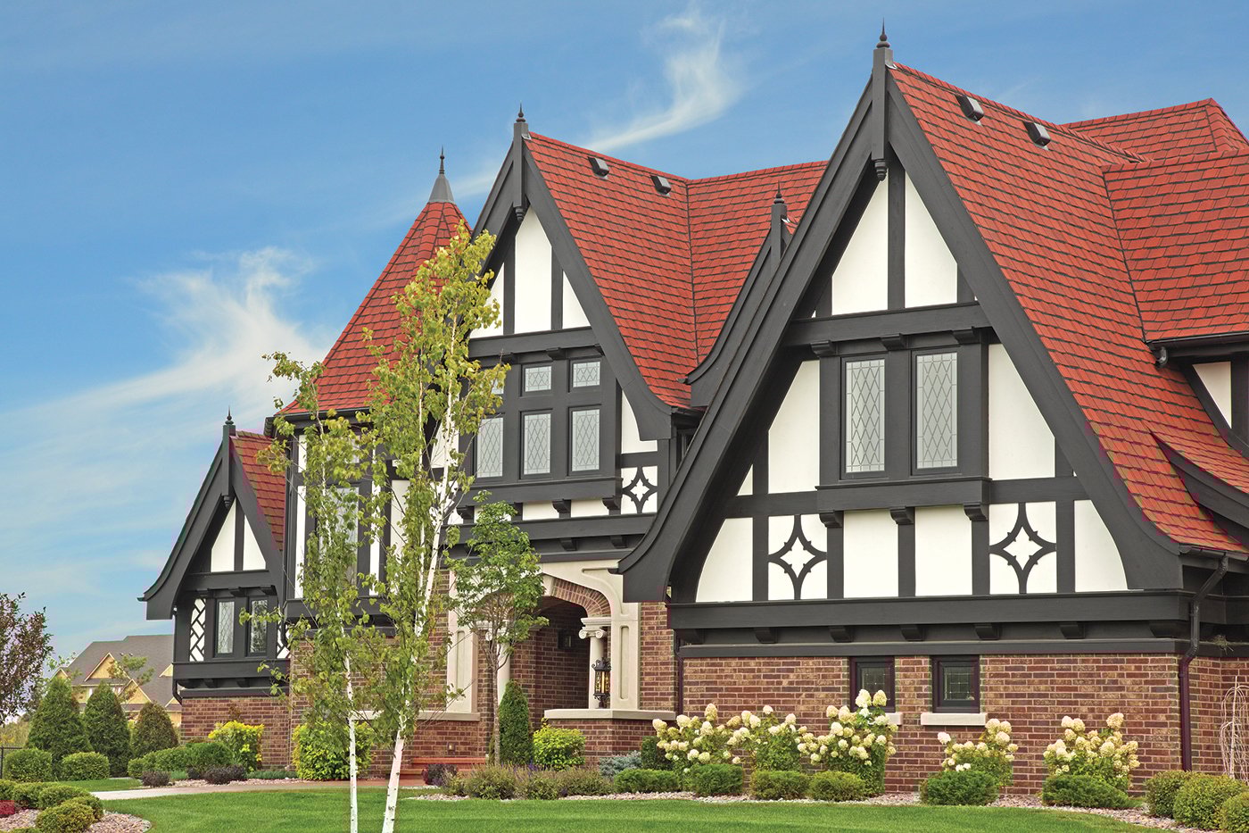 An exterior shot of a Tudor home with red roof, multiple gables, and black half-timbering over white stucco.