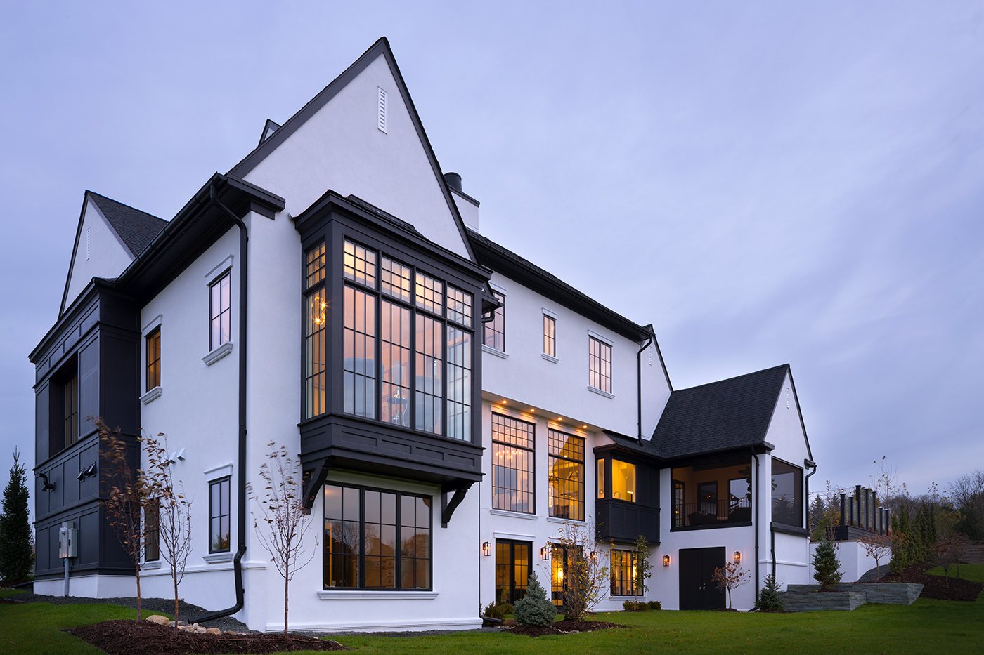 A home with white stucco and black roof, several gables, and a large rectangular bay window.