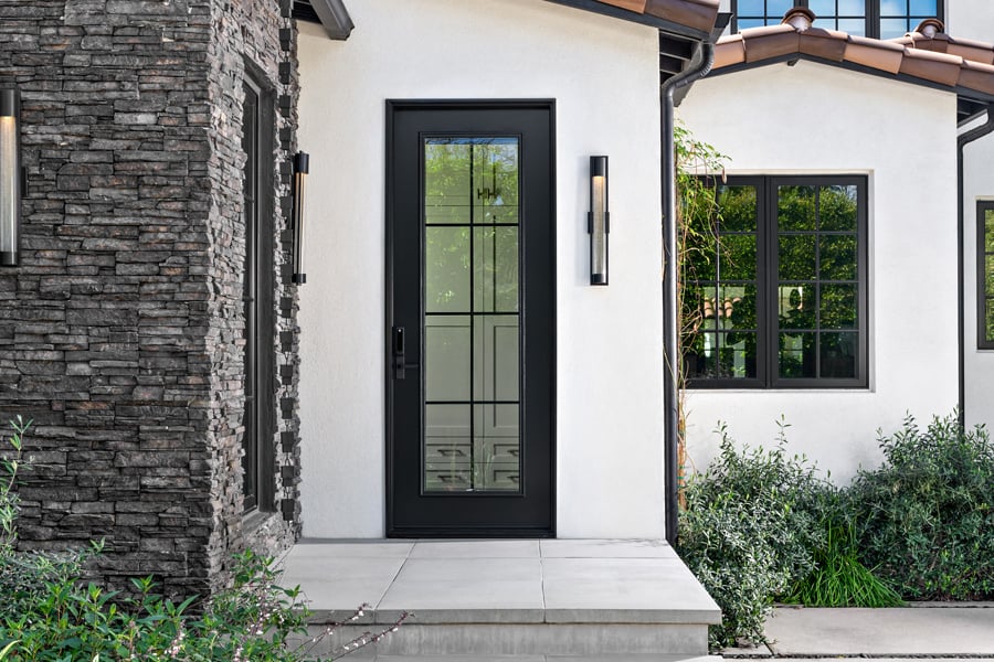 A Spanish-style entrance to a home with grey stone and white stucco walls and black windows and doors with colonial grilles.