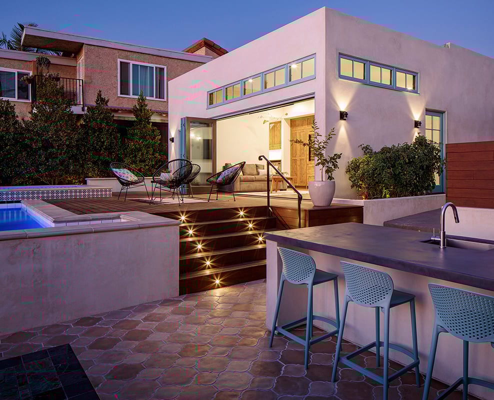 An outdoor living area with a bar and pool leading into a Spanish-style home with a Folding Outswing Door and aquamarine-colored E-Series windows. 