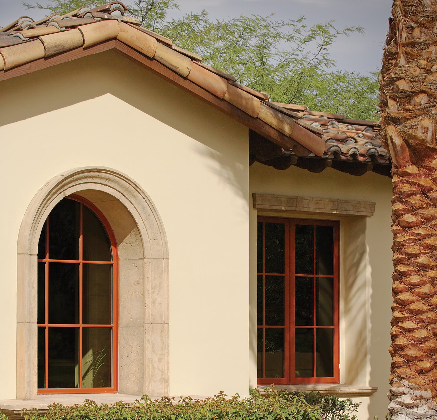 Casement windows on a Spanish-style home with a red tile roof and palm tree in front.