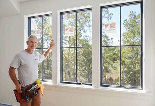 A contractor stands next to a bank of newly installed windows.