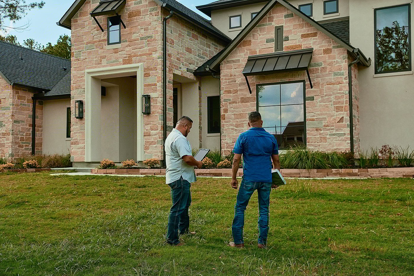 Two men stand in front of a freshly sodded new construction home.