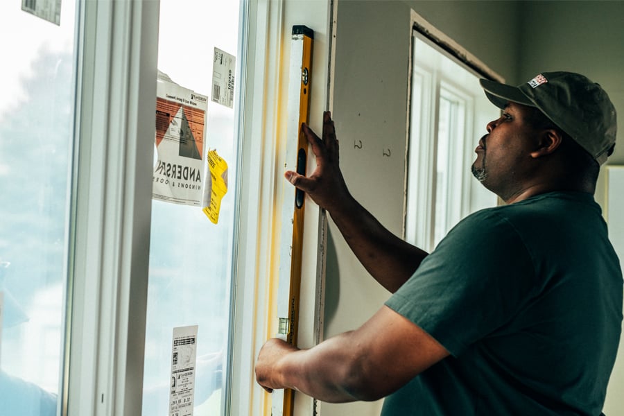A contractor holding a level checks that the window he’s installing is plumb.