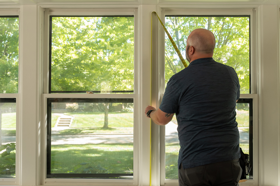 A contractor measures a window for replacement.