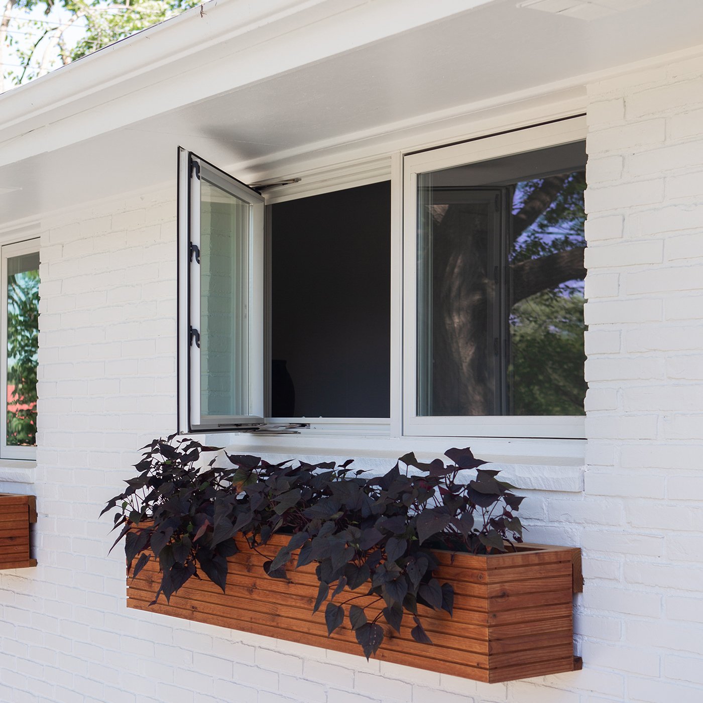 A wood window box underneath a 100 Series Casement Window on a white brick Ranch home.