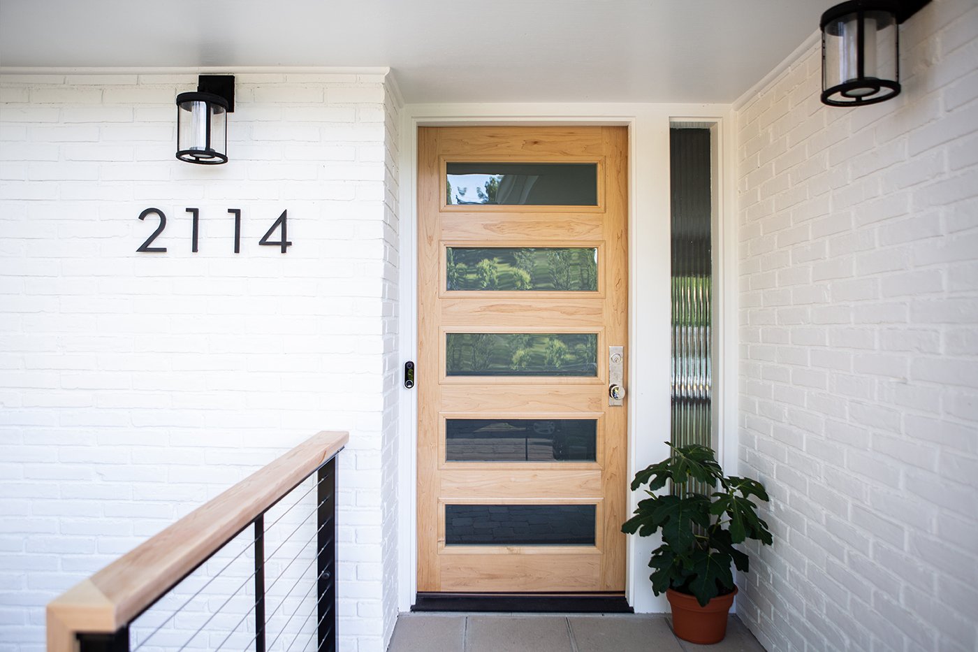 A white-painted brick Ranch home with a natural wood front door 